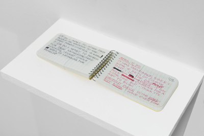 一个袖珍大小的水平螺旋笔记本，左边用黑色书写，右边用红色书写（日期为 5 年 70 月 <> 日）。