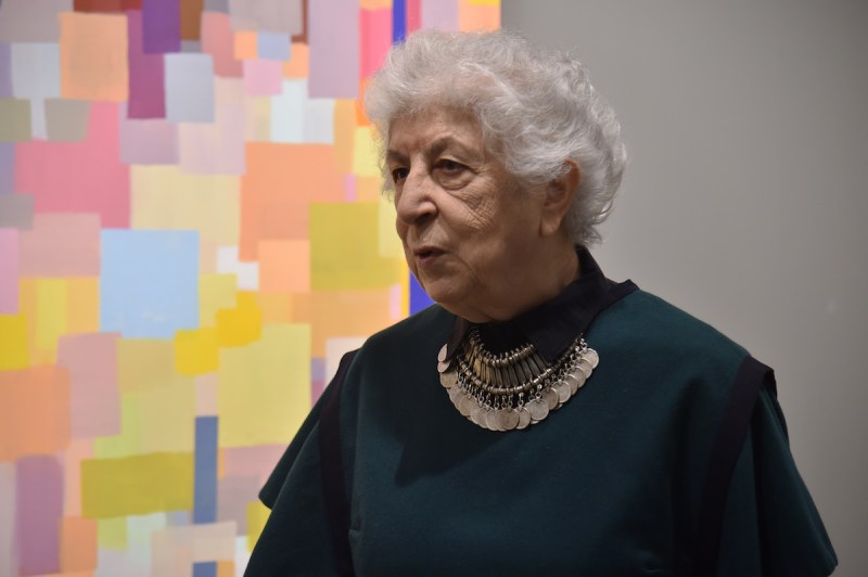 一个女人站在一幅抽象画旁边，画上有许多叠加的彩色方块。